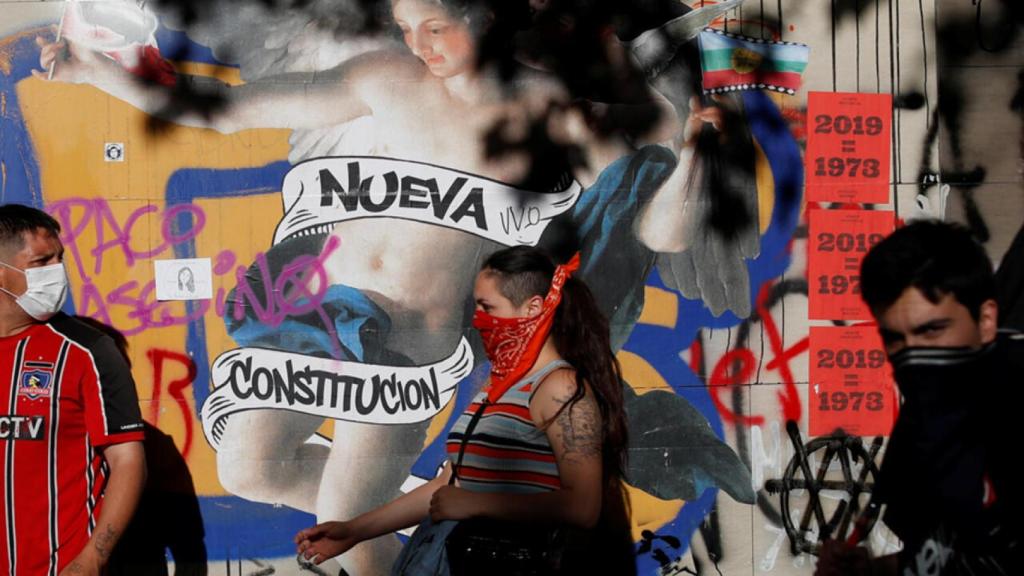 Manifestantes ante un graffiti que dice Nueva Constitución en noviembre de 2019.