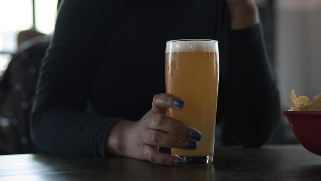 Una mujer bebe una cerveza sola.