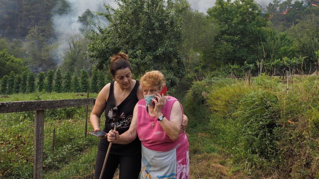 Una anciana llama por teléfono con el incendio de Folgoso do Courel (Galicia) de fondo.