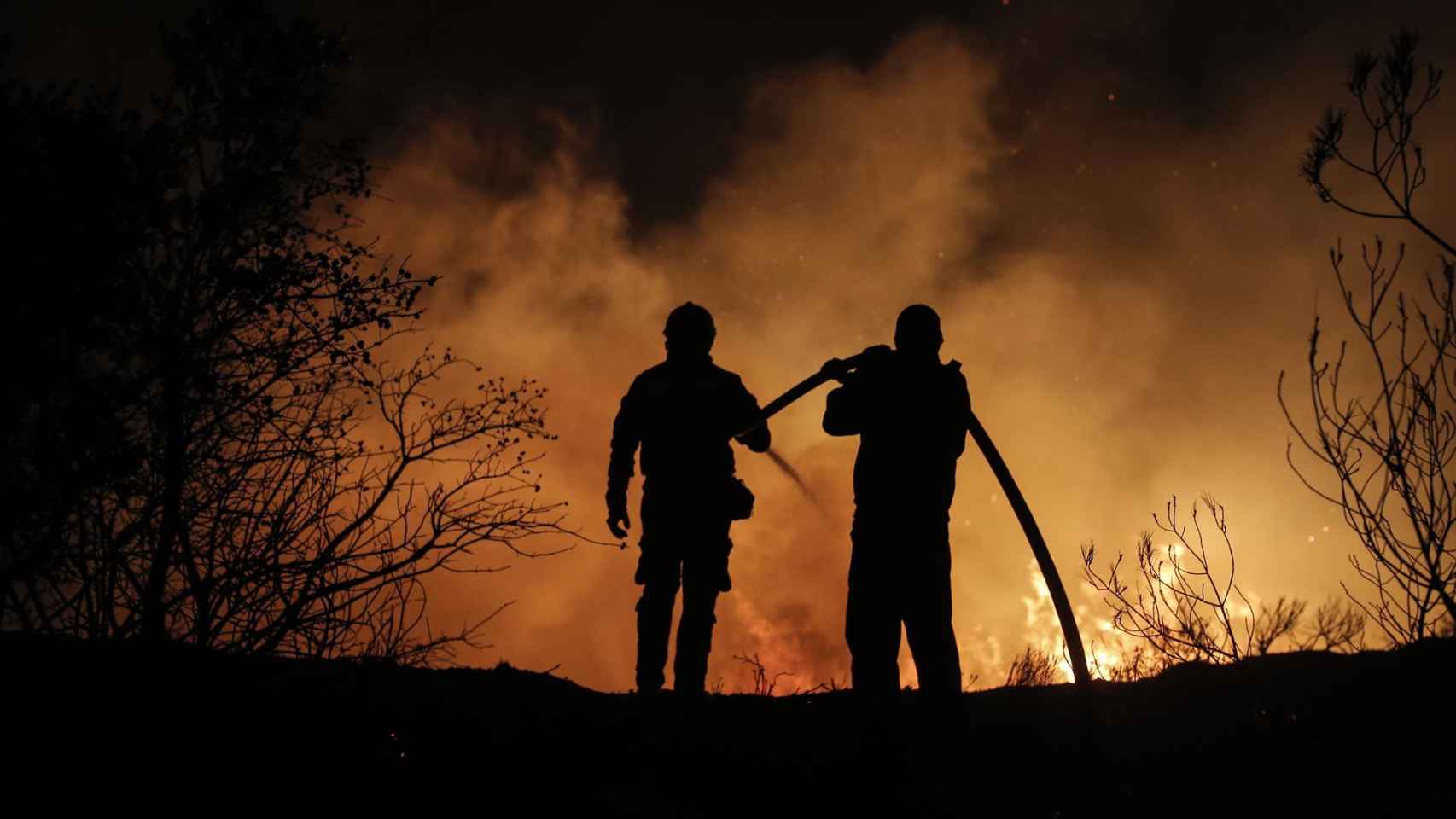 Dos bomberos trabajan en las labores de extinción de un fuego.