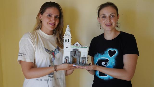 Las ecuatorianas Constanza Vela (I) participante en la ruta Quetzal en 2021 junto a su hermana Montserrat posan con la reproducción de la iglesia de Santo Domingo de Quito realizada por su tío que han encontrado durante las tareas de catalogación para el futuro museo de Miguel de la Quadra en Santervás de Campos