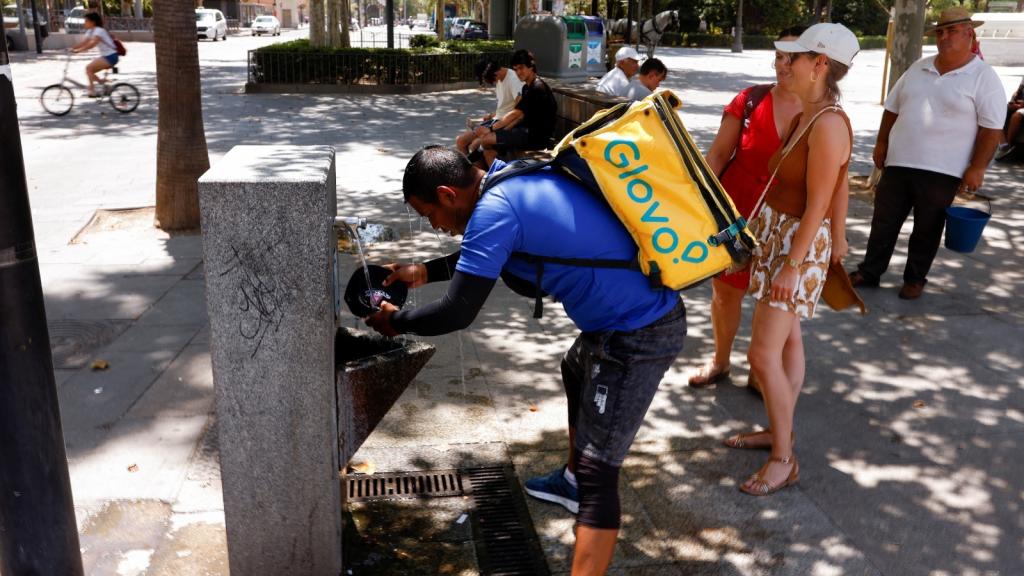 Un trabajador de Glovo se refresca en una fuente en Sevilla el pasado 11 de julio.