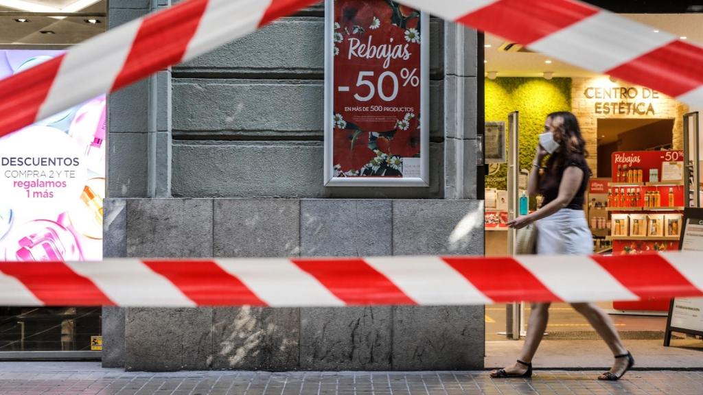 Una persona protegida con mascarilla pasa al lado del escaparate de una tienda donde se observan carteles indicativos de rebajas en Valencia, Comunidad Valenciana (España).