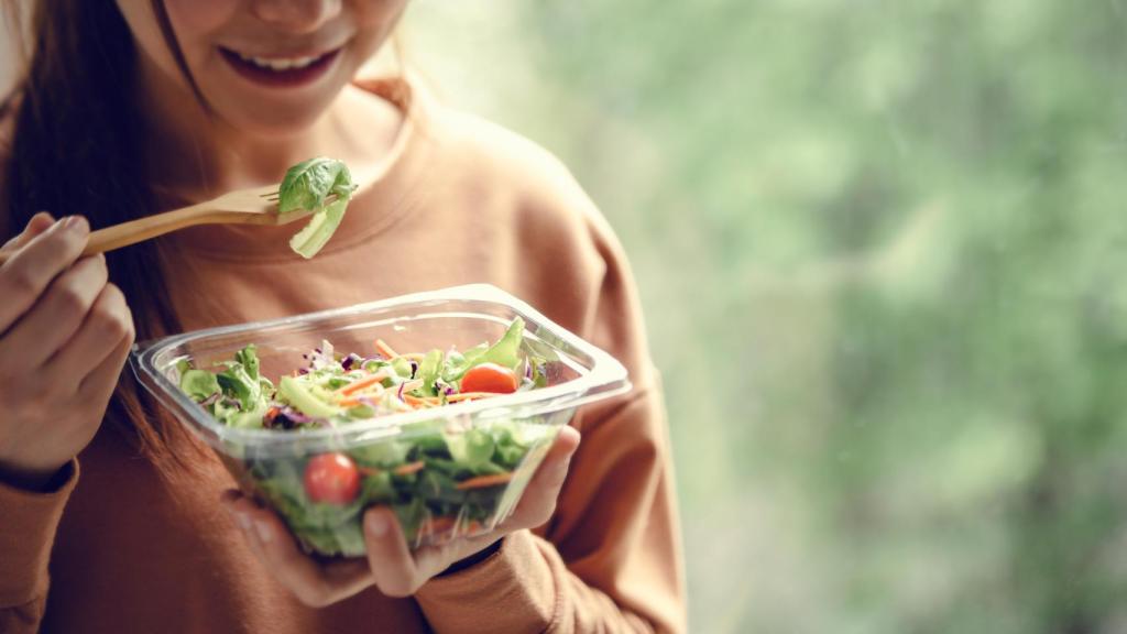 Una mujer come una ensalada en un envase de plástico.