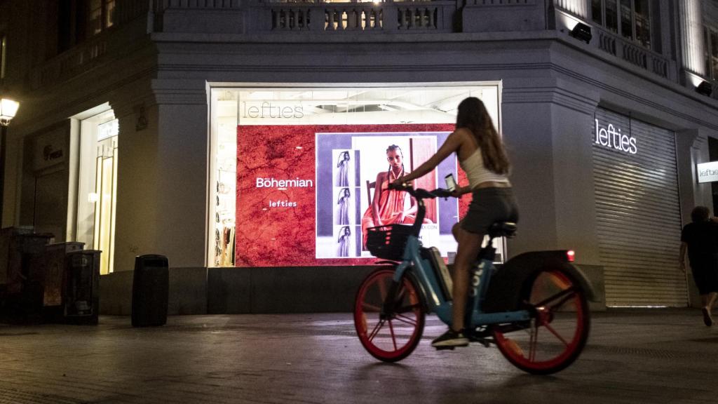 Una chica pasea con su bicicleta con los carteles iluminados de fondo.