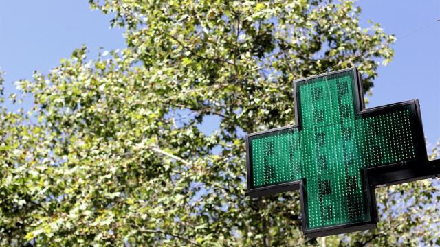 Una señal luminosa de la cruz verde a la entrada de una farmacia.