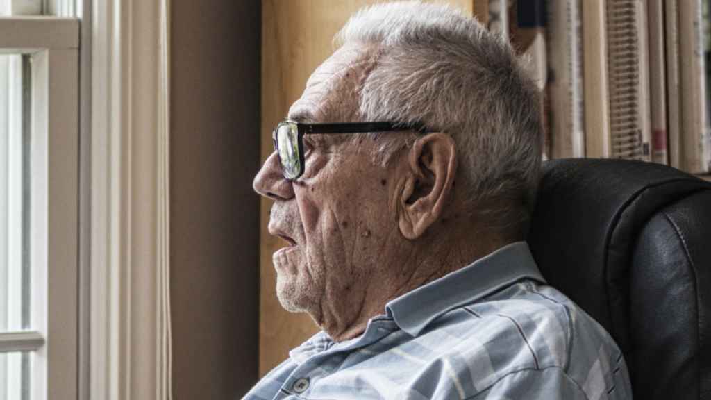 Un anciano mirando a través de una ventana.