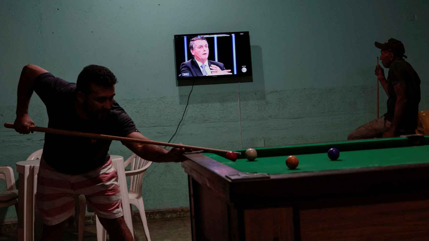 Ciudadanos brasileños juegan al billar mientras Bolsonaro aparece en televisión.