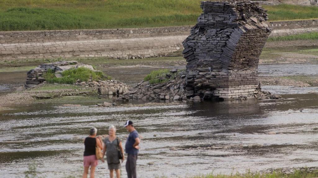 Tres personas junto al río Miño, cuyo bajo caudal ha dejado a la vista las ruinas del antiguo Portomarín.