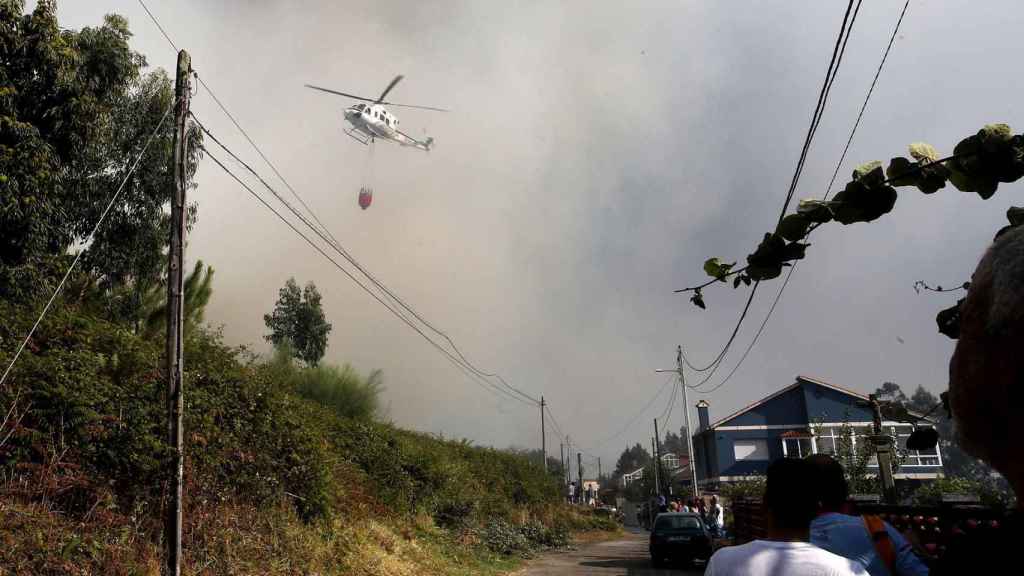 Un helicóptero entre el humo trabaja con una cuba de agua en el incendio, a 22 de agosto, en la parroquia de Meira.
