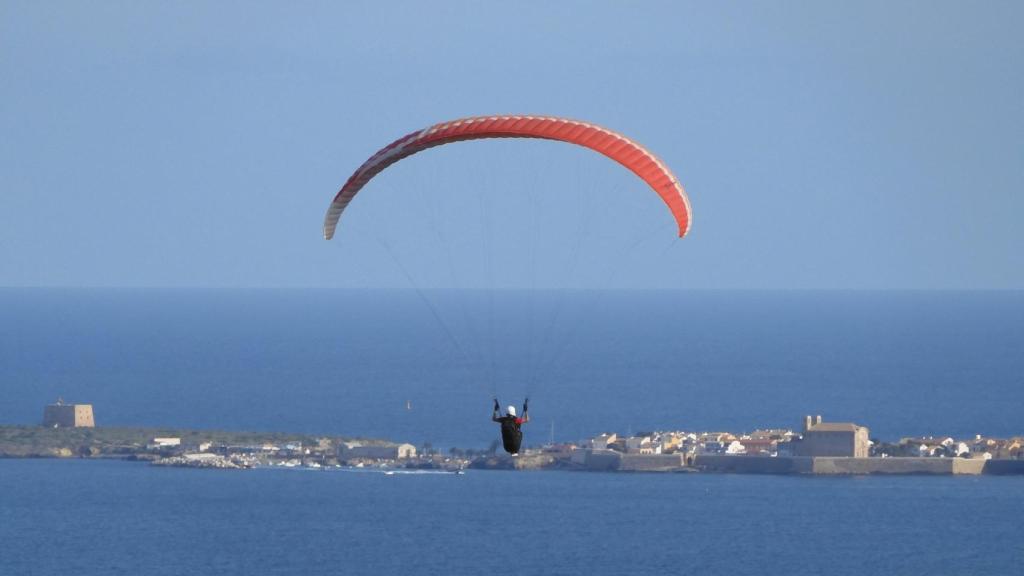 Un parapentista sobrevuela el cabo de Santa Pola, con la isla de Tabarca al fondo.