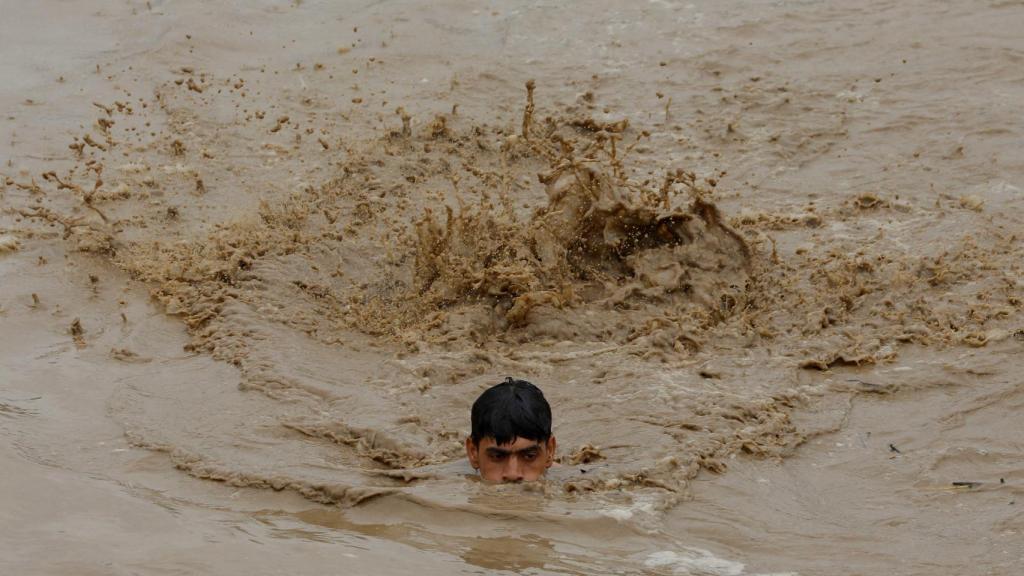Un hombre nada para salvar la vida en las inundaciones en la localidad de Charsadda, en Pakistán.