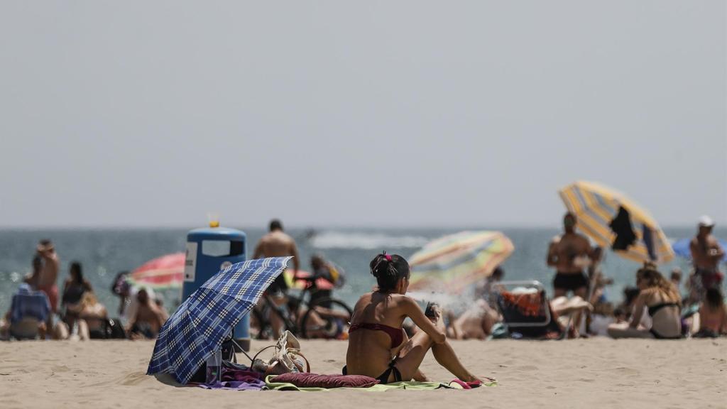 Personas tomando el sol en una playa valenciana, en imagen de archivo.