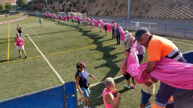 Decenas de voluntarios cargan con el gran lazo rosa en el campo de fútbol de Trillo.