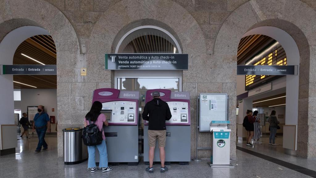 Dos personas compran billetes en los cajeros de venta automática en la estación de trenes.