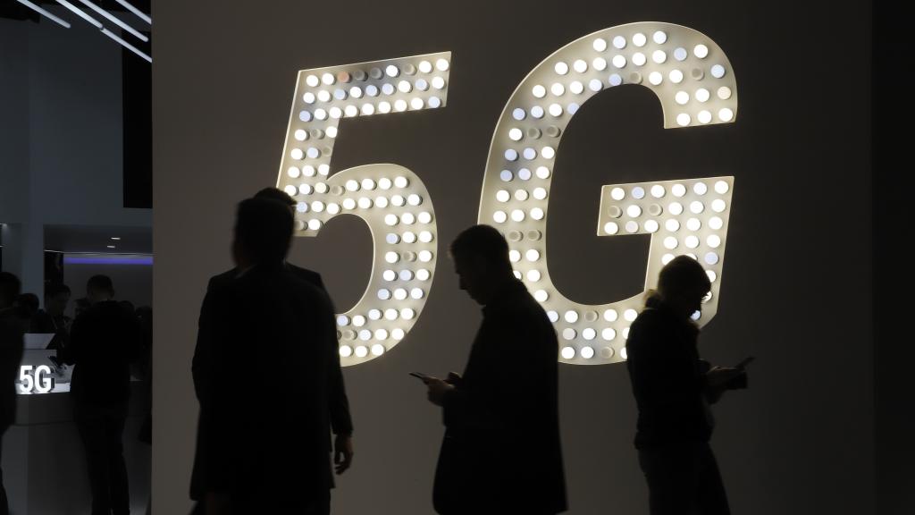 Varias personas mirando su teléfono móvil delante de un luminoso del 5G.