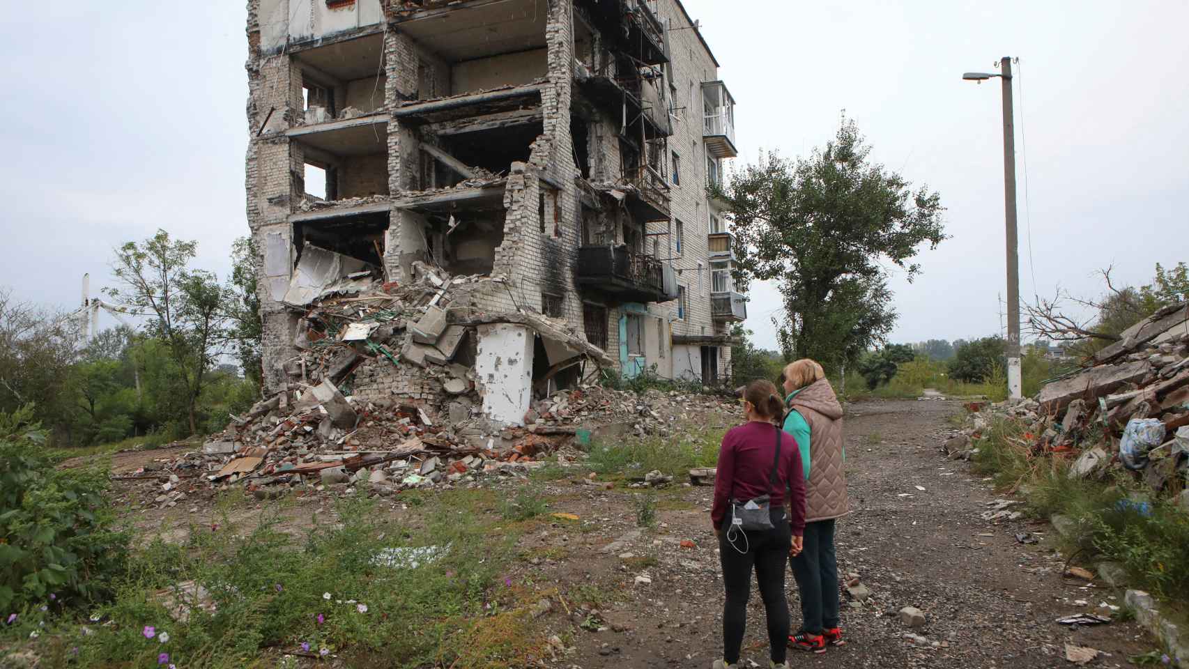Las mujeres se paran cerca de un edificio residencial destruido por un ataque militar en la ciudad de Izium.