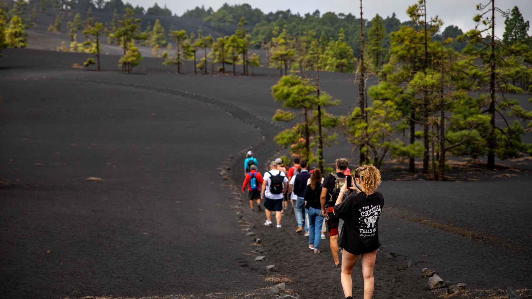 Turistas caminan por un sendero afectado por la lava del volcán de Tajogaite.