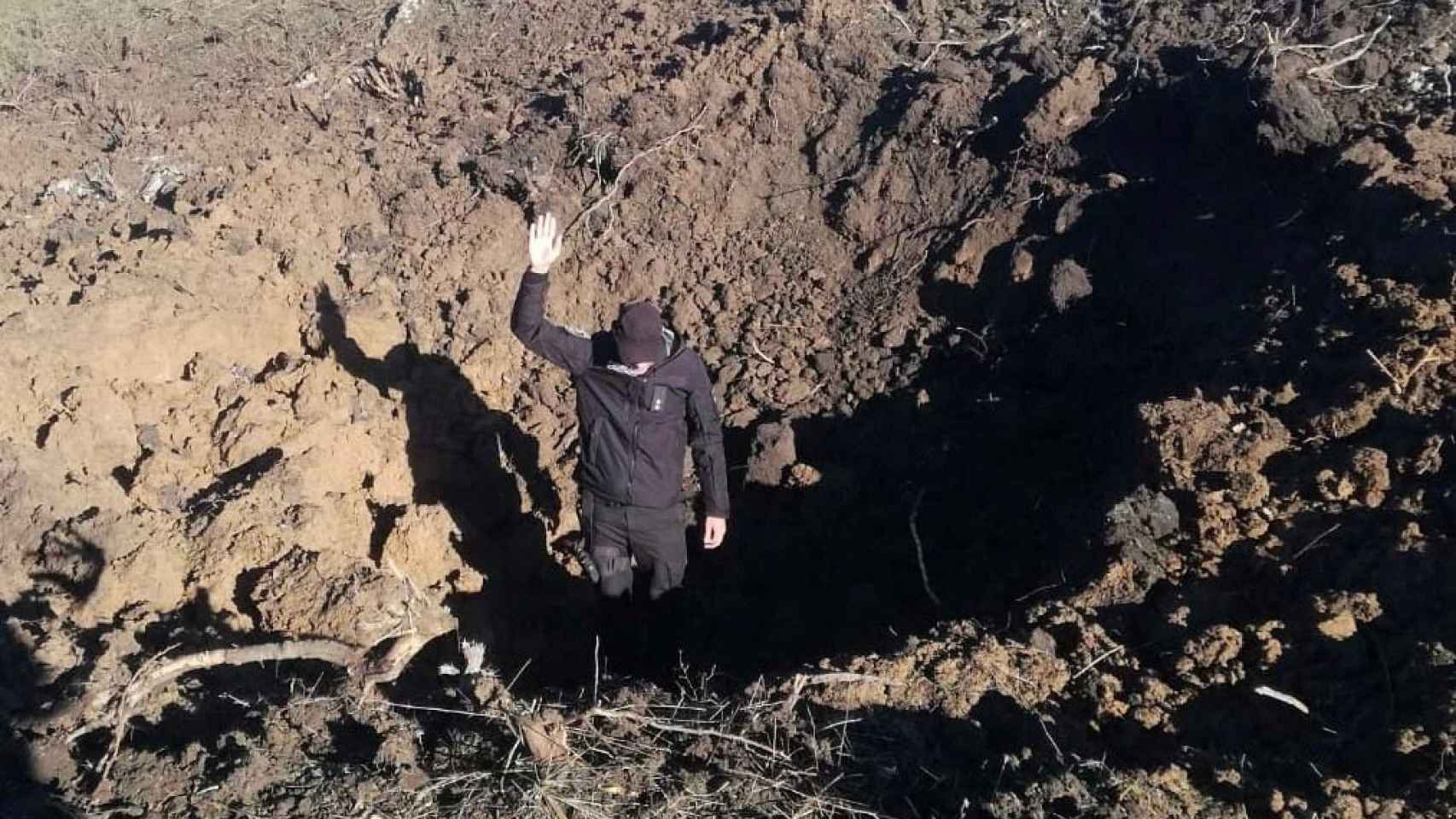 Un oficial de policía se para en el fondo de un cráter de proyectil dejado por un ataque militar ruso en un complejo de la planta de energía nuclear de Pivdennoukrainsk en Yuzhnoukrainsk