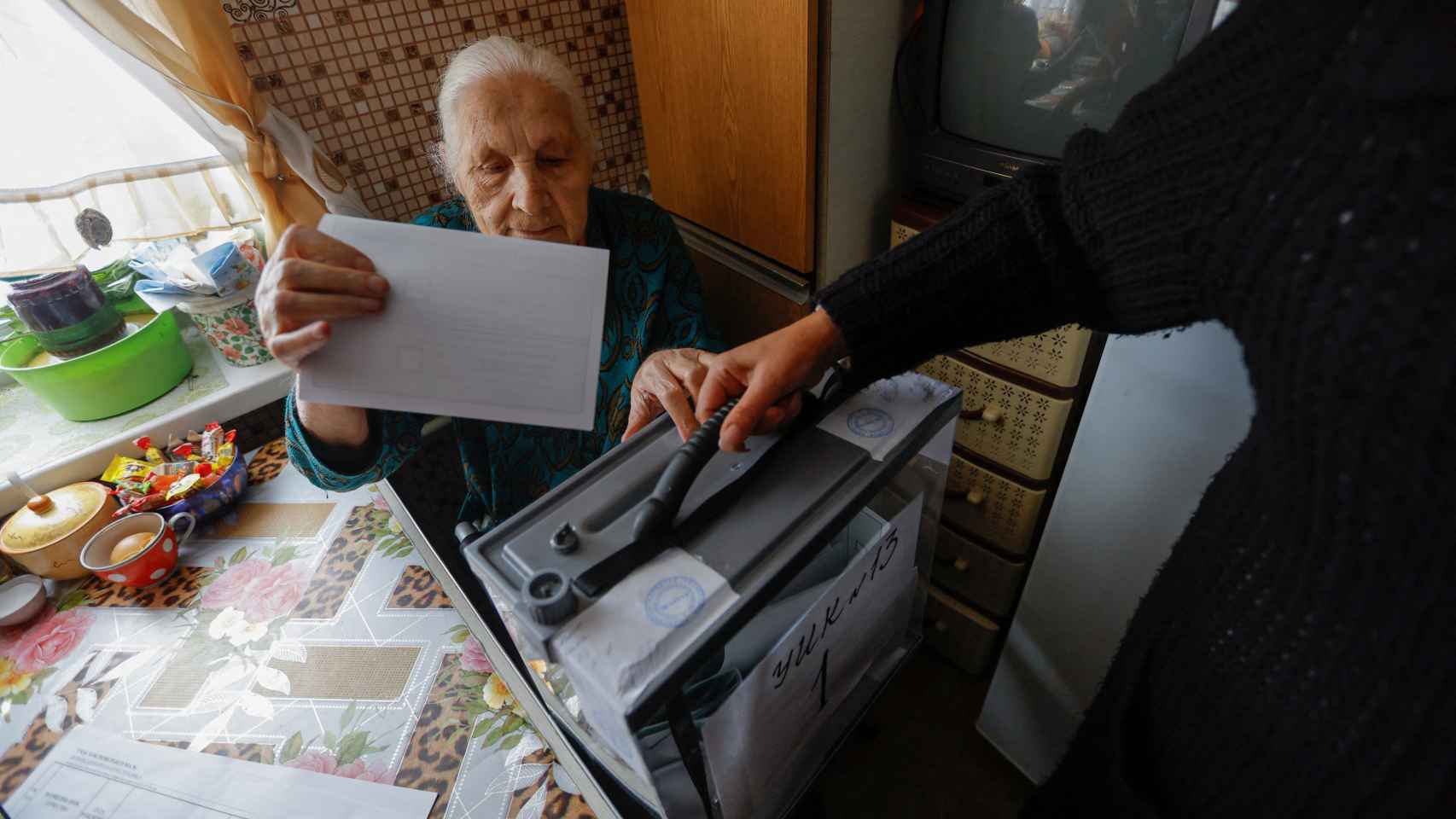 Una ciudadana de Mariúpol deposita su voto mientras los miembros de una comisión electoral entran en los apartamentos con una urna portátil.
