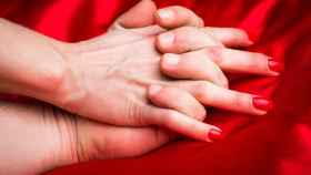 La manos de una pareja sobre una sábana de seda roja.