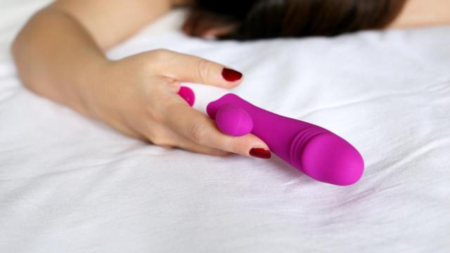 La mano de una mujer en la cama que sujeta un vibrador.