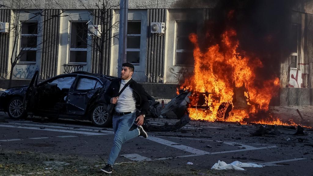 Un joven huye de los coches en llamas en del centro de Kiev tras el ataque ruso de este lunes.