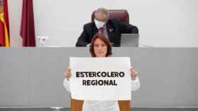 María Marín, portavoz de Podemos, este miércoles, con un mono y un cartel denunciando que la Asamblea Regional es un estercolero.