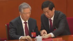 Hu Jintao  intenta ver unos documentos de la carpeta roja pero Li Zhanshu se lo impide.