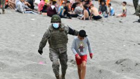 Un militar español acompaña a un niño marroquí en la playa de Ceuta que ha entrado a España de forma ilegal.