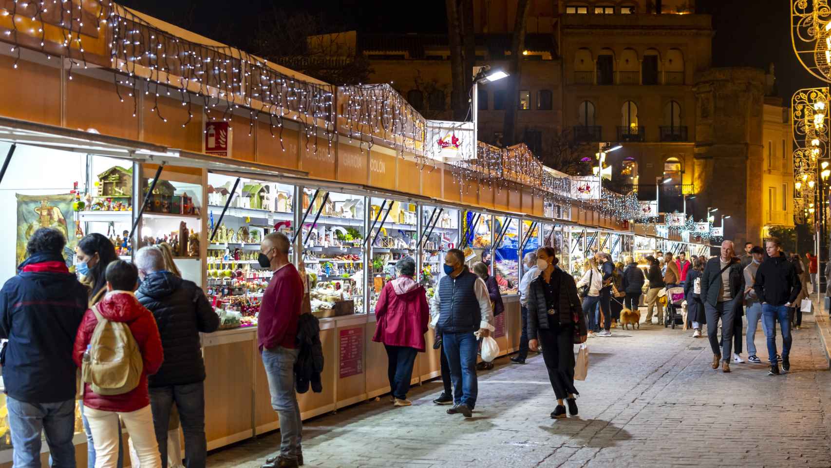 Turistas y españoles locales visitan un puesto de mercado navideño cerca de la catedral en una noche de invierno en el centro histórico de Sevilla, España.