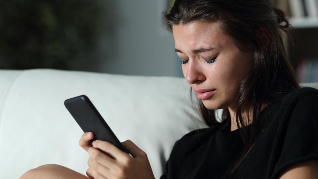 Una chica joven llora mirando su móvil.