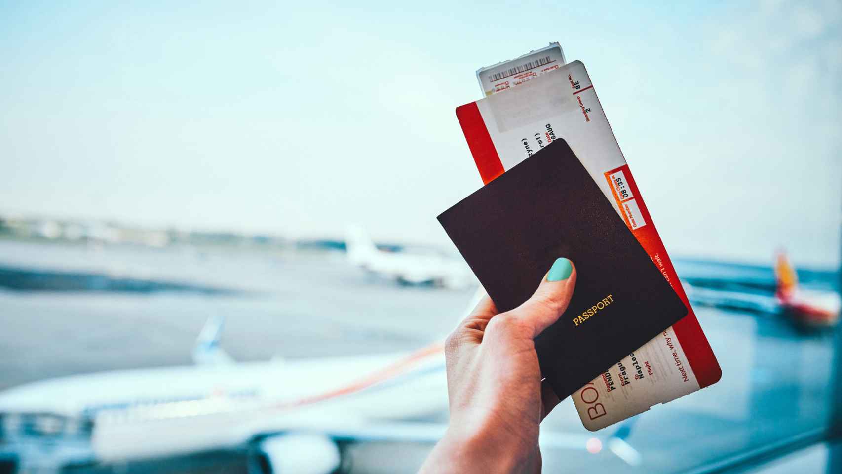 Una mano de una mujer en un aeropuerto con un pasaporte y billete de avión.