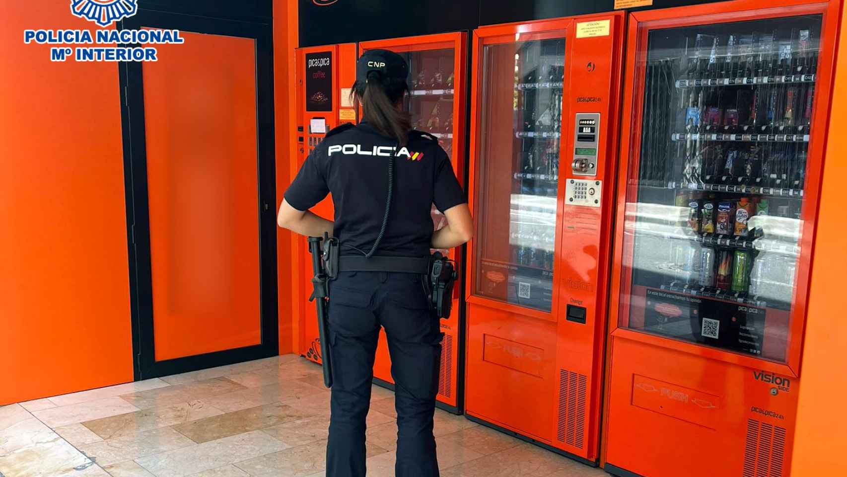 Una agente de la Policía Nacional junto a unas máquinas expendedoras en Elche.