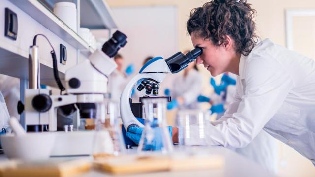 Una mujer investigadora mira por un microscopio.