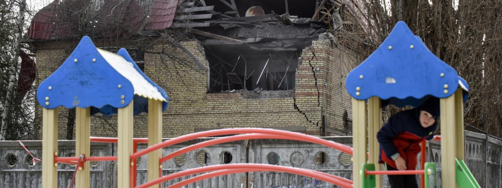 Un niño juega en un parque infantil junto a un edificio destruido por las bombas en Kiev.