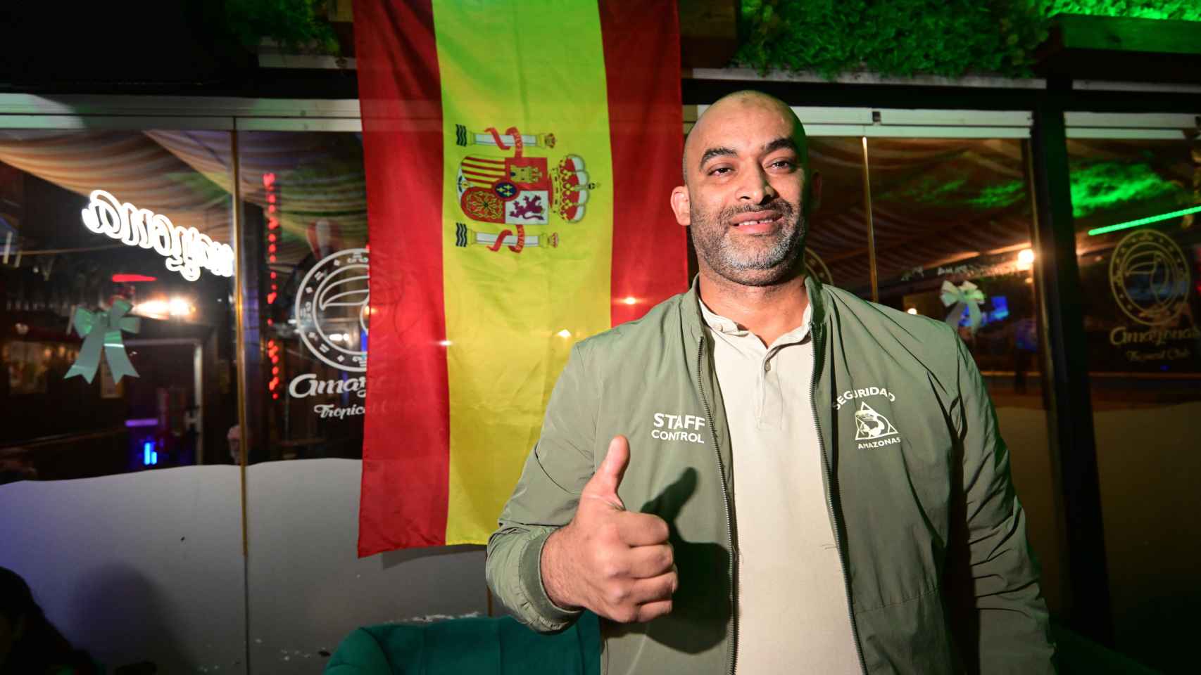Raschid, encargado de seguridad, posa junto a la bandera de España que cuelga en el local.