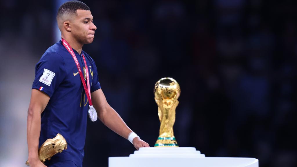 Kylian Mbappé, con la Bota de Oro del Mundial de Qatar 2022 pasando junto al trofeo de la Copa del Mundo