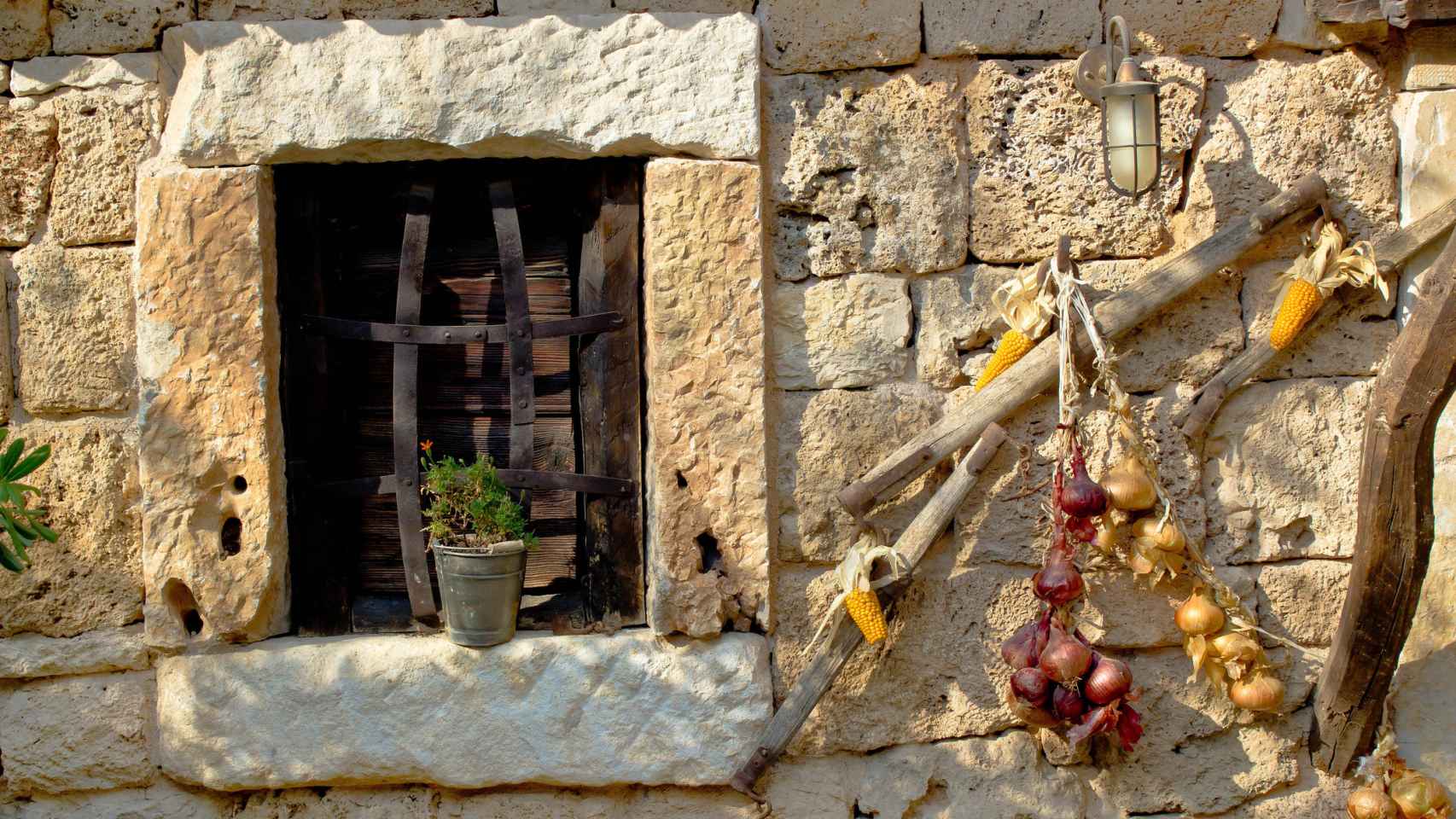 Imagen de archivo con cebollas colgando al lado de la ventana de una casa de piedra.