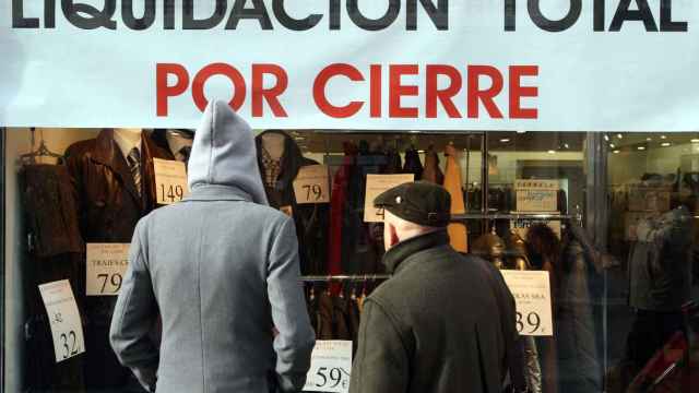 Dos hombres miran el escaparate de un establecimiento que anuncia su cierre en Valladolid