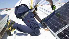 Un operario instalando unas placas solares sobre un tejado para autoconsumo.