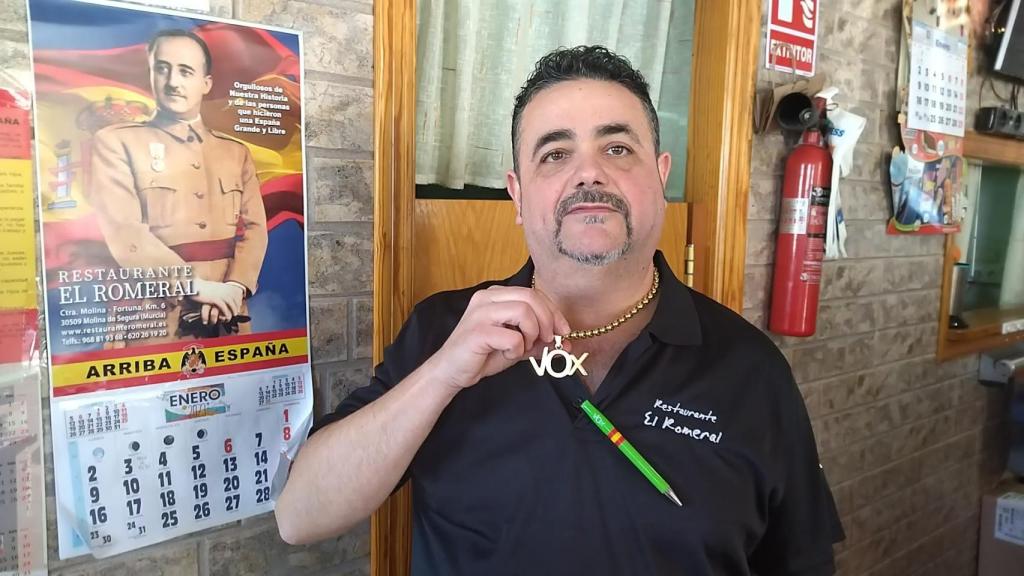 El hostelero David Gomariz posa con su uniforme y su insignia de Vox, junto a su calendario franquista, en el restaurante que regenta en Molina de Segura.