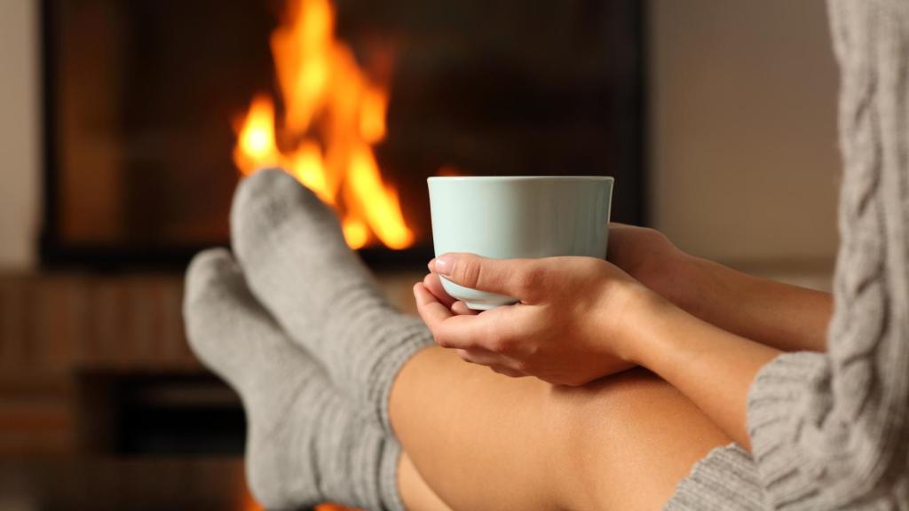 Una mujer toma un café junto a la chimenea.