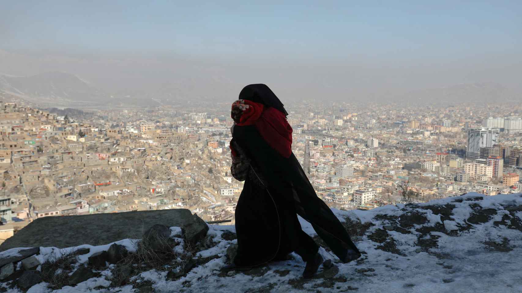 Una mujer carga con su hijo en brazos vestida con burka desde un mirador con vistas a Kabul (Afganistán)
