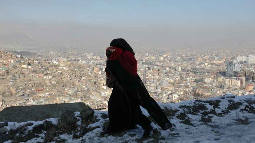 Una mujer carga con su hijo en brazos vestida con burka desde un mirador con vistas a Kabul (Afganistán)