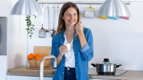 Una mujer joven comiendo yogur mientras está de pie en la cocina de casa