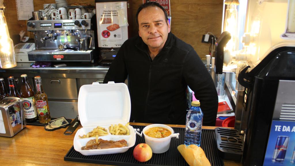 Carlos de la Torre, en su bar, posando junto al menú del día más barato de España.