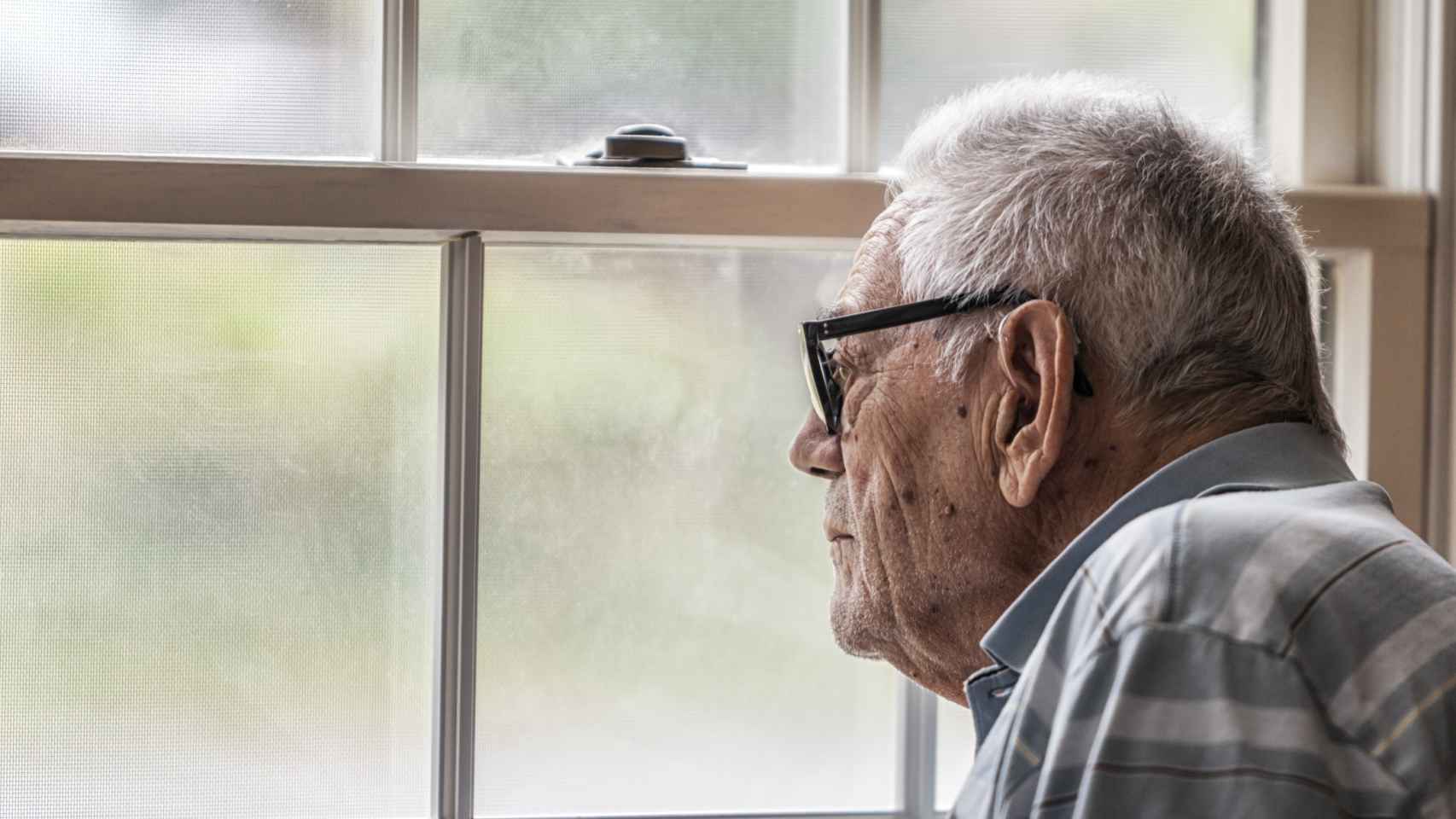 Un anciano con la enfermedad de Alzheimer mirando a través de la ventana.
