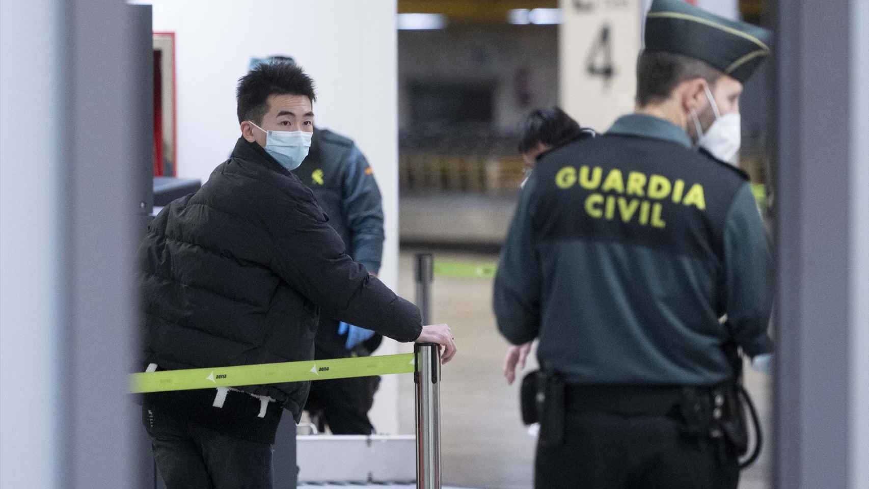 Un pasajero de origen asiático camina por la terminal 4 del aeropuerto Madrid-Barajas frente a un agente de la Guardia Civil