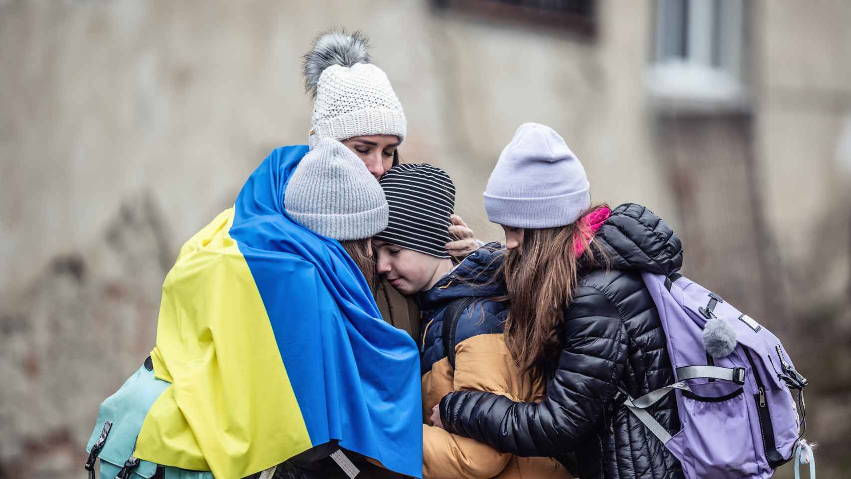 Una mujer se abraza con su familia rodeada por una bandera de Ucrania.